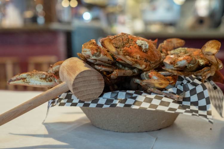 blue crabs covered in seasoning sitting in paper bowl with mallet resting on side