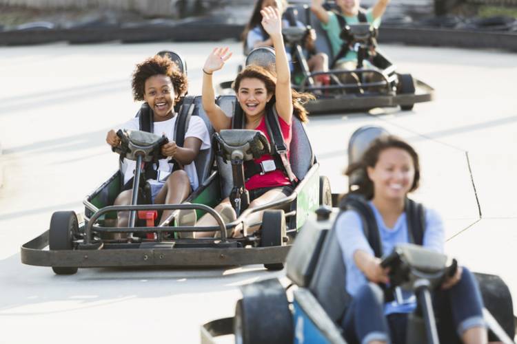 Multi-ethnic teenage girls riding go carts at amusement park. Focus on two girls in middle (16 years).